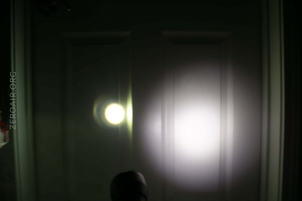 A dimly lit door with two distinct light spots, one small and bright on the left, and one larger and softer on the right, cast onto the door. The faint outline of an object appears at the bottom center.
