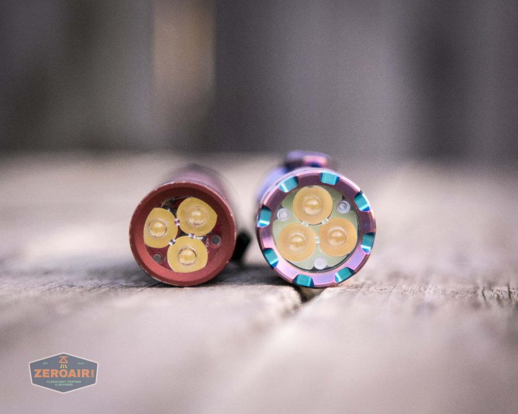 Two cylindrical flashlight heads with three yellow LED emitters each are shown side by side on a wooden surface, viewed from the front. The flashlight on the right has a colorful bezel.