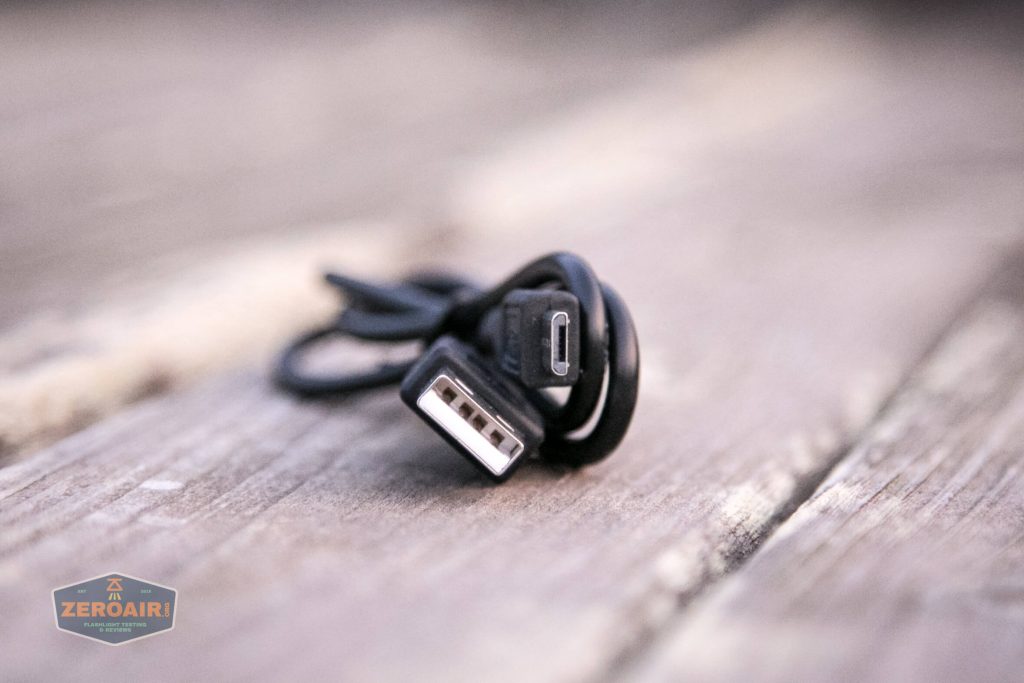 A close-up view of a black cable with a USB-A connector and a USB-C connector, coiled and resting on a weathered wooden surface. The background is blurred, and a ZeroAir logo appears in the bottom left corner.