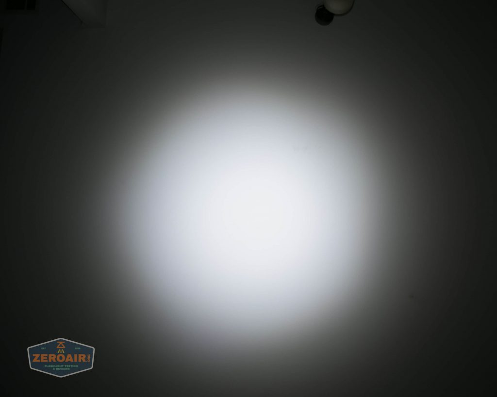A circular beam of white light is projected onto a dark surface, creating a bright central spot with fading edges. There is a small ZeroAir logo in the bottom left corner of the image.
