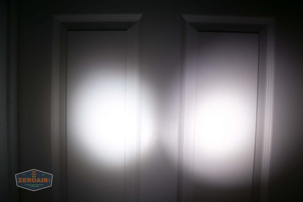 Two bright flashlight beams shine side by side on a white paneled door in a dark environment. The beams create circular patterns and overlap slightly at the center.