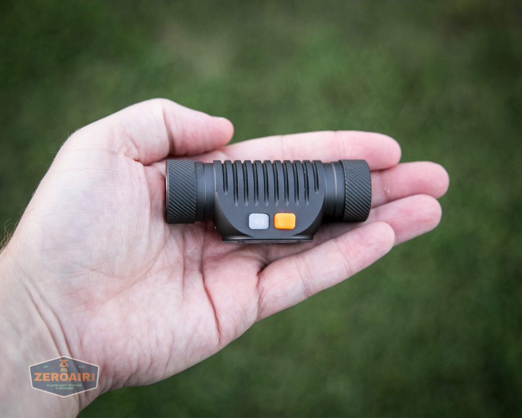 A hand holding a compact black flashlight with ribbed sides and two buttons, one gray and one orange, against a blurred outdoor background. The ZeroAir logo is visible in the lower left corner.