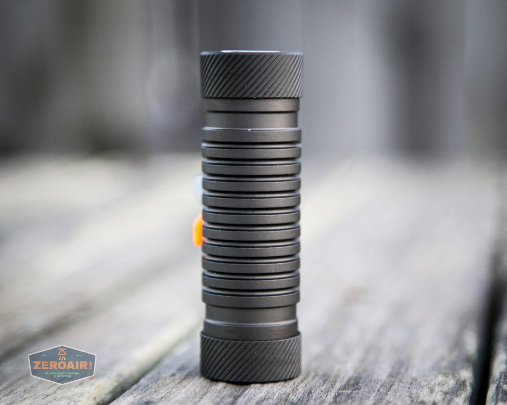 A compact, cylindrical black flashlight with grooved grips stands upright on a wooden surface. The background is blurred and the ZeroAir logo is visible in the bottom left corner.