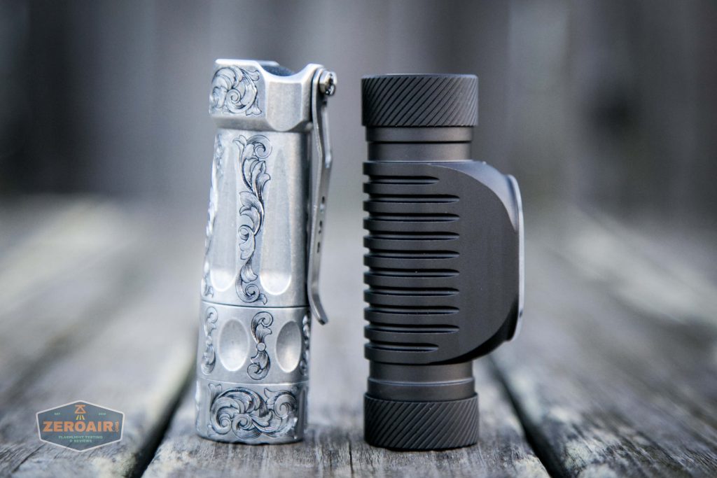 Two small flashlights stand upright on a wooden surface; the left one is silver with ornate engravings, and the right one is black with a ribbed texture and a side clip. A ZeroAir watermark appears in the lower left corner.