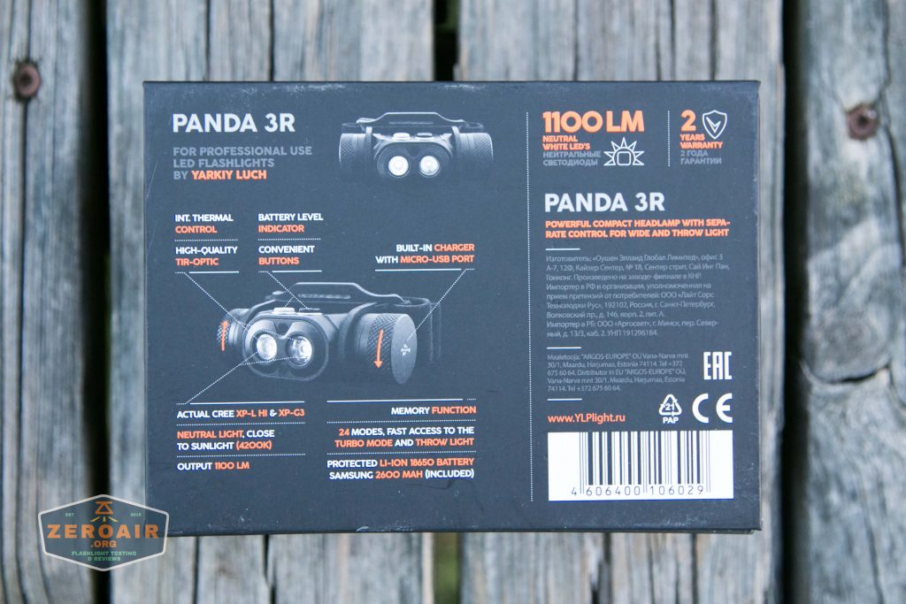 A black product box for the Panda 3R LED flashlight, showing technical specifications, features, and branding, placed on a weathered wooden surface. The box mentions 1100 lumens, 2-year warranty, and built-in USB charging.