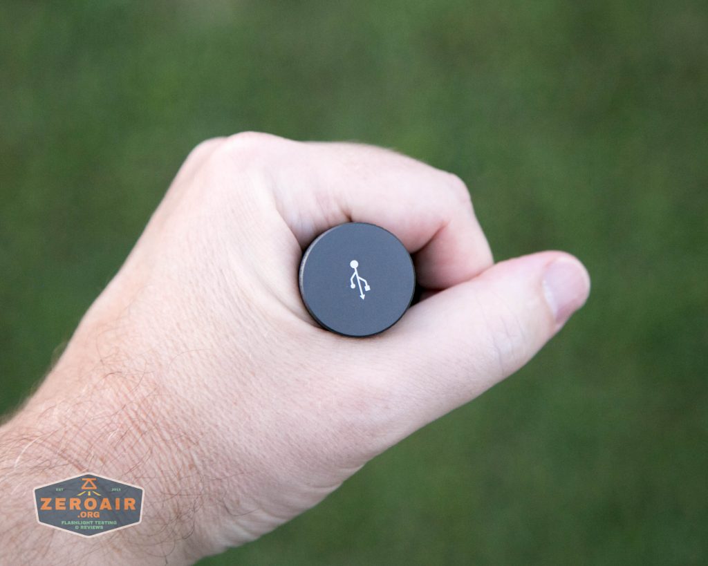 A hand holds a cylindrical black object vertically, displaying a white walking person icon on the top. The background is green and blurred. A “ZEROAIR” watermark appears in the lower left corner.