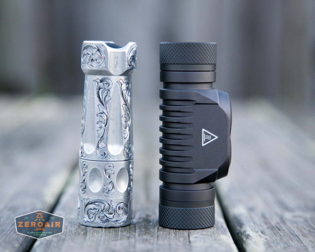 Two compact flashlights stand upright on a wooden surface. The left flashlight is silver with ornate, engraved patterns, while the right flashlight is matte black with a textured grip and a logo. A ZeroAir logo is in the lower left corner.