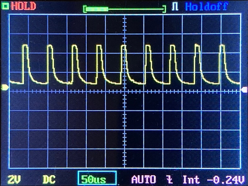 A digital oscilloscope screen displays a repeating yellow waveform with sharp peaks and regular intervals. Horizontal gridlines denote voltage; vertical gridlines denote time. Settings: 2V/div, 50μs/div, DC coupling.