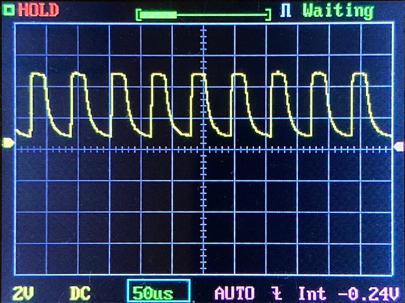 Oscilloscope screen displaying a repeating waveform pattern with five distinct peaks per cycle. The settings show 2V/div, 50 microseconds/div, and a DC coupling mode. Display statuses read HOLD and Waiting.