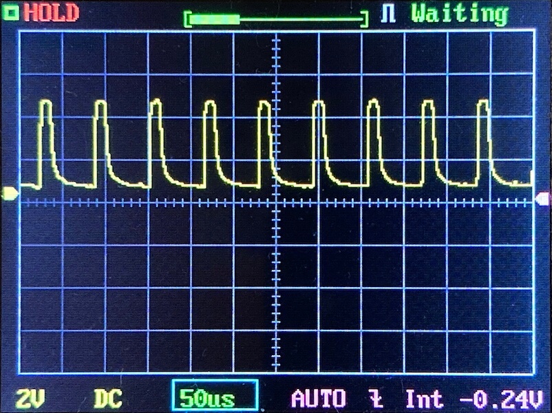 An oscilloscope screen displays a repeating yellow waveform with sharp peaks and intervals. The horizontal scale reads 50 microseconds per division, and the vertical scale is set to 2 volts per division. Various settings are visible.