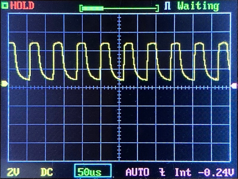 An oscilloscope display shows a periodic yellow waveform with sharp peaks and rounded troughs. The horizontal scale is 50 microseconds per division, and the vertical scale is 2 volts per division. Various settings are visible.