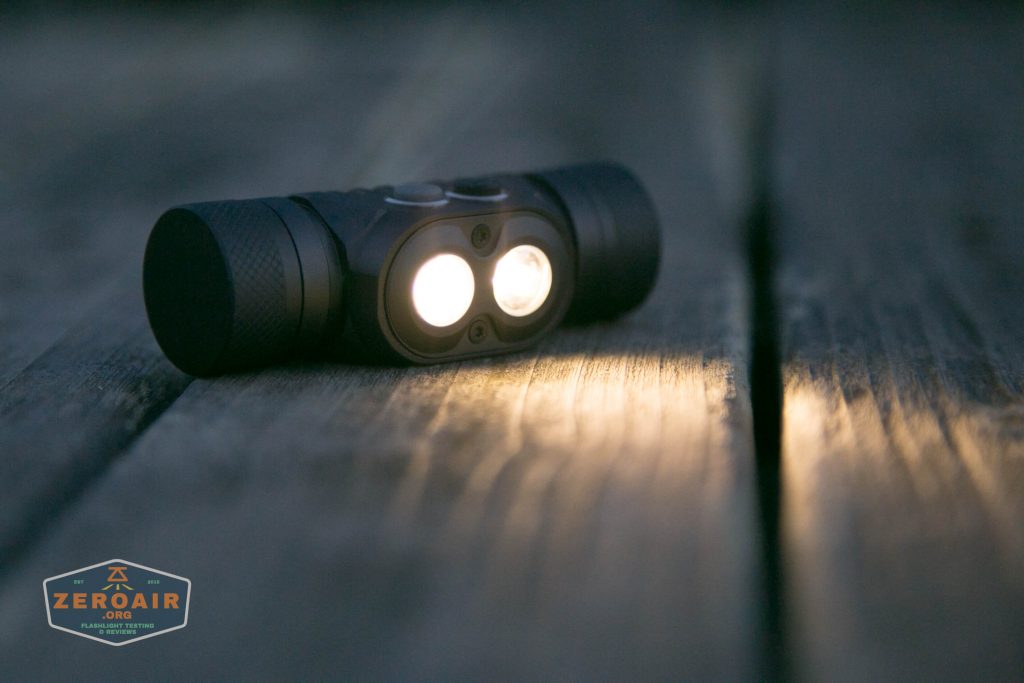 A small black flashlight with two illuminated lenses rests on a weathered wooden surface, casting light in opposite directions. The ZeroAir logo is visible in the bottom left corner.