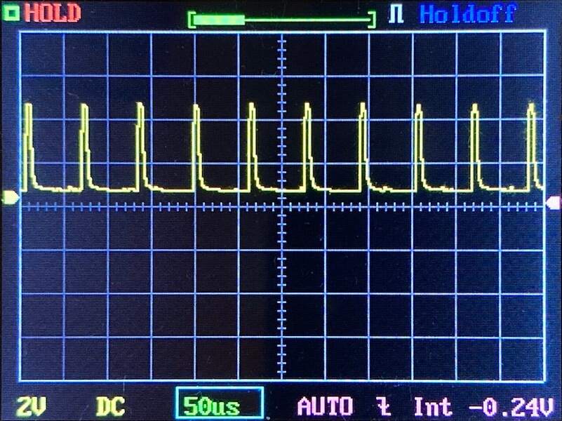 Oscilloscope screen displaying a repeating yellow waveform with sharp peaks and intervals on a grid. Settings at the bottom show 2V, DC, 50µs, AUTO, Int, and -0.24V adjustment.
