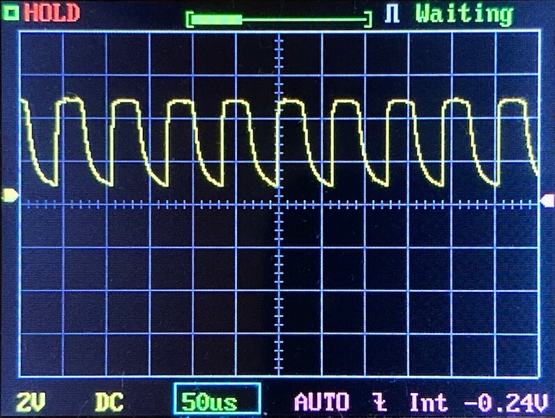 An oscilloscope screen displays a yellow waveform with a repeating, irregular pattern. The settings show 2V per division vertically, 50 microseconds per division horizontally, with the measurement in DC mode.