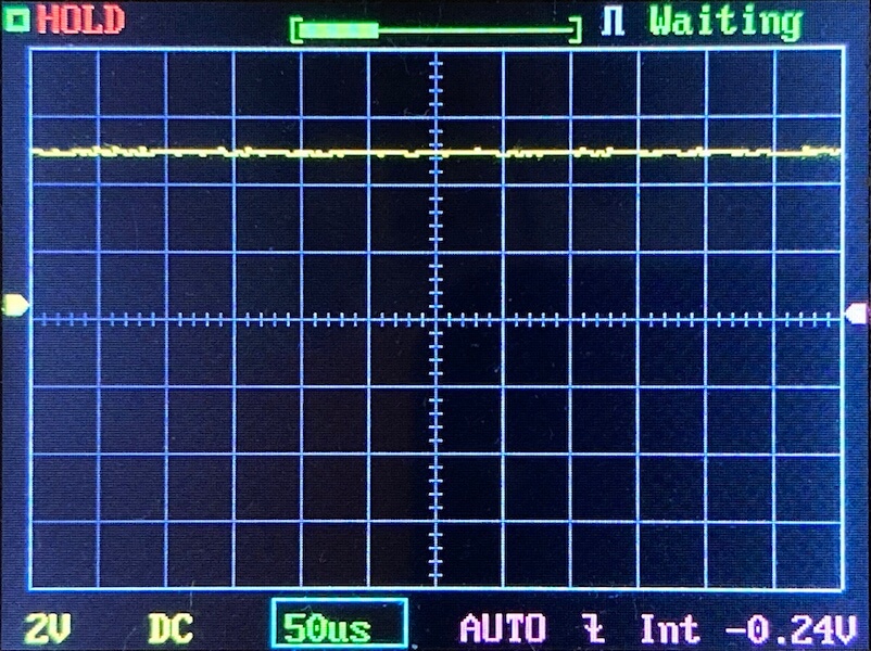 An oscilloscope screen displays a mostly flat yellow waveform near the center, with gridlines and measurement settings shown below: 2V, DC, 50µs, AUTO, and -0.24V. The status reads HOLD and Waiting.