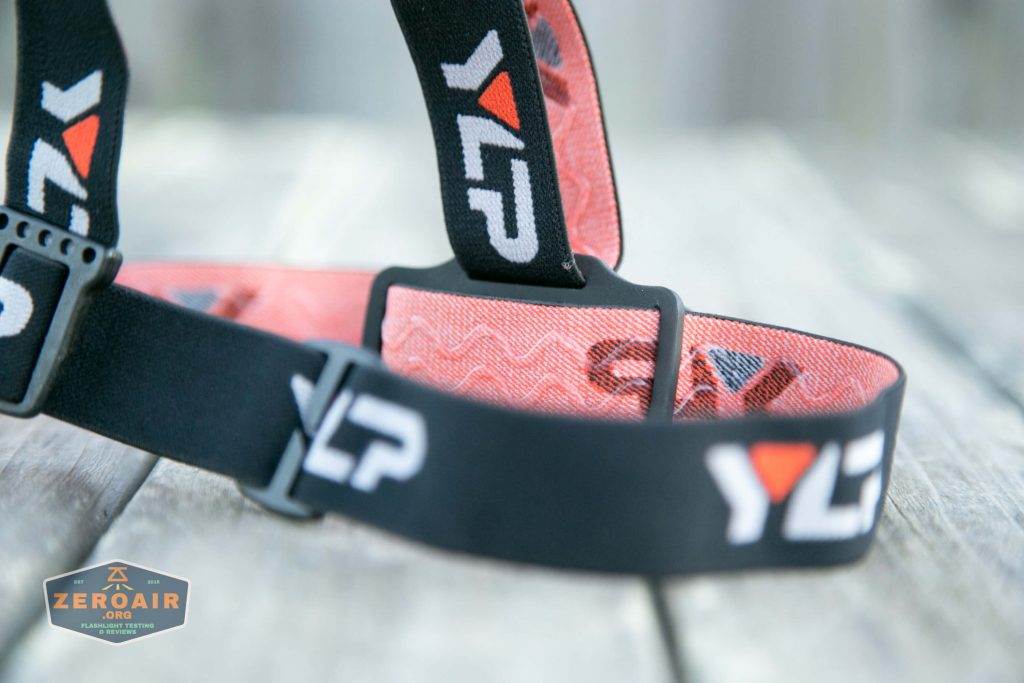 A close-up of a black and orange adjustable strap with YLP printed in white and orange. The strap is resting on a wooden surface, and a ZeroAir.org logo is visible in the lower left corner.