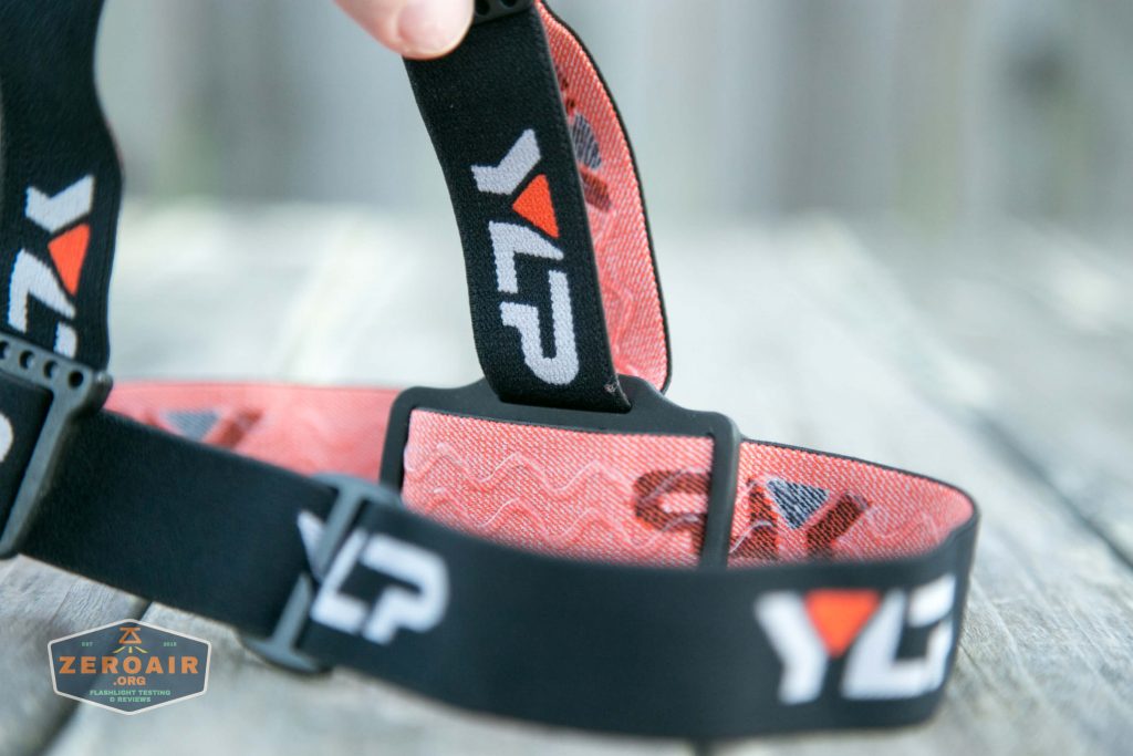 Close-up of a black and red elastic headband with the letters YLP printed in white and orange. The band is looped and resting on a weathered wooden surface, with a ZeroAir logo in the corner.