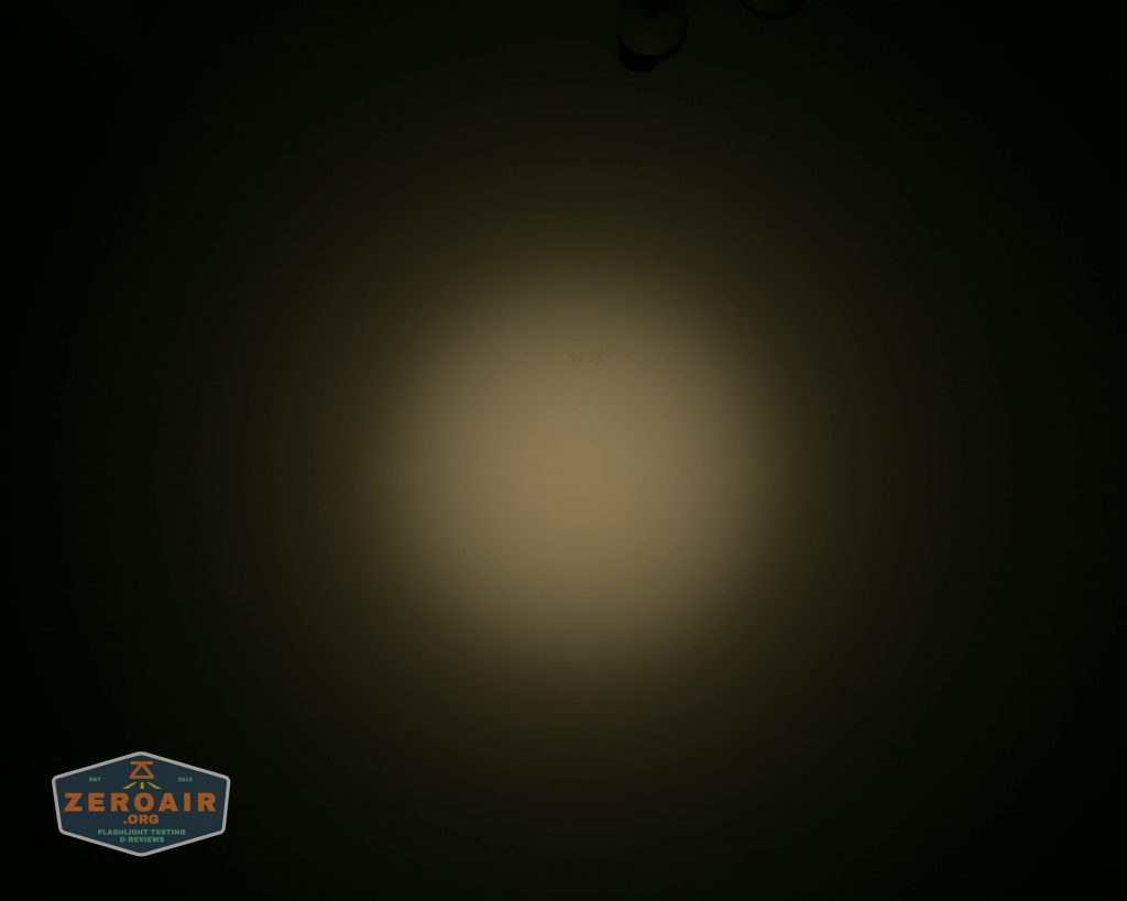 A dim circular beam of light is projected onto a dark surface, creating a soft gradient from bright center to darker edges. A small ZeroAir logo appears in the bottom left corner.