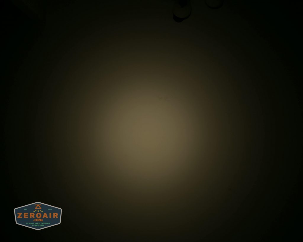 A dim circular light beam is projected onto a dark surface, with the ZeroAir logo visible in the bottom left corner. The rest of the image is mostly dark, with faint outlines near the top edge.