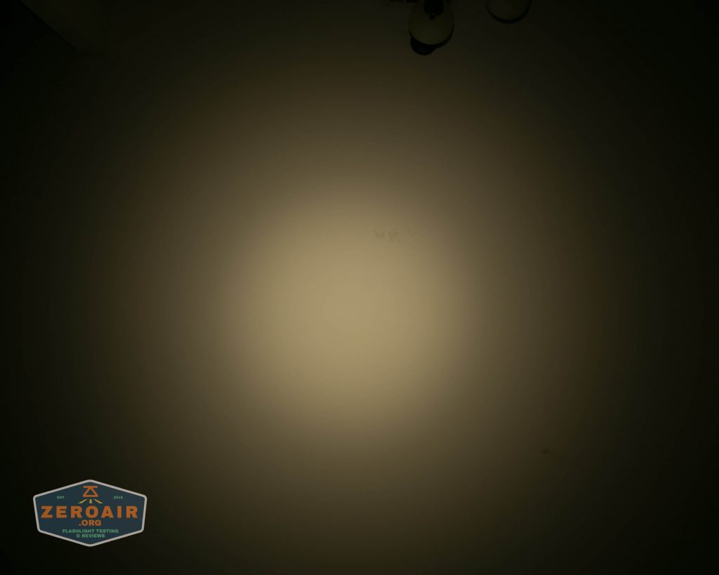 A circular beam of light is projected onto a blank wall in a dark room. The light creates a gradient effect, brighter in the center and fading towards the edges. A ZeroAir logo appears in the lower left corner.