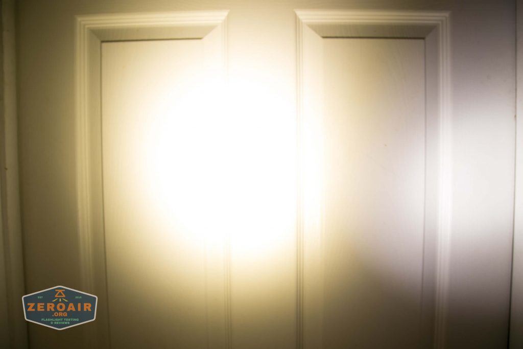 A bright flashlight beam shines on a white, paneled door, creating a circular area of intense light in the center. A logo in the lower left corner reads ZEROAIR.ORG.