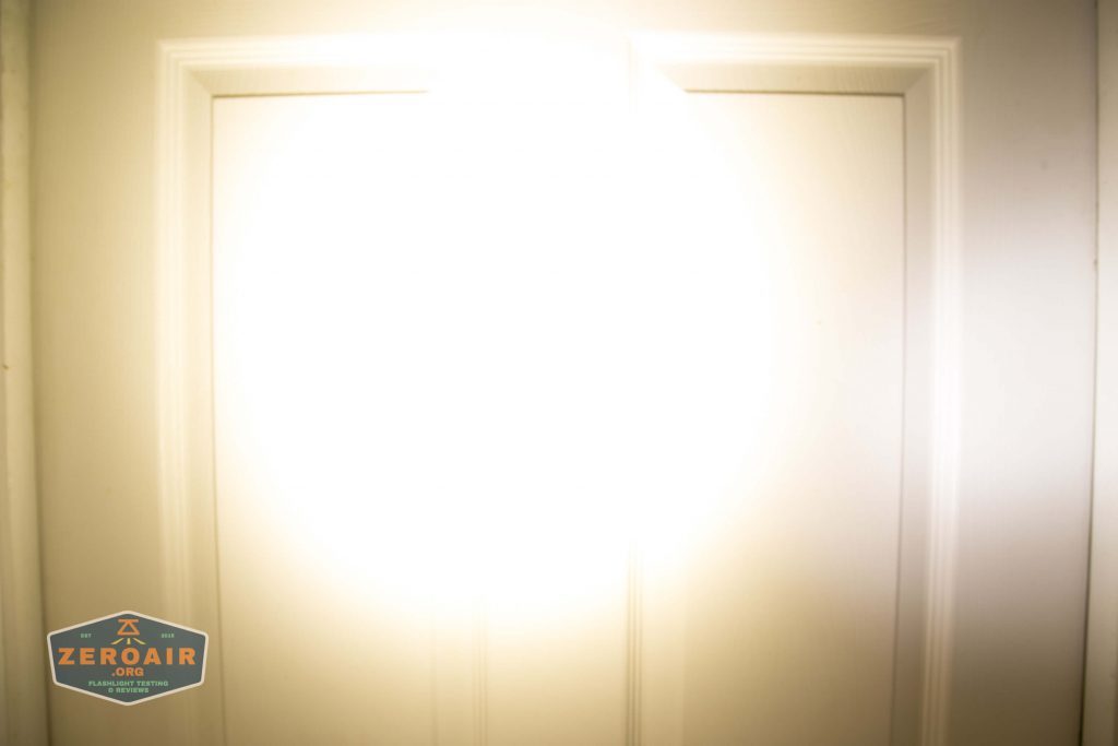 A bright flashlight beam shines directly onto a closed white door, creating a large, circular, overexposed area in the center. A small logo in the bottom left corner reads ZeroAir.