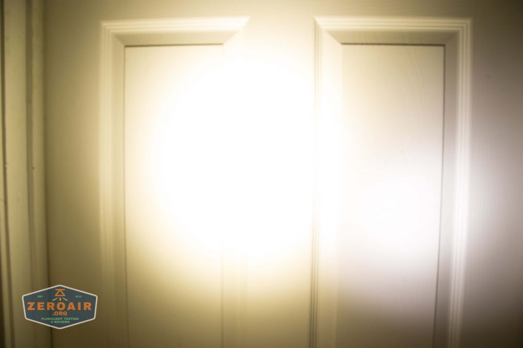 A bright flashlight beam is shining directly onto a white paneled door, creating a large area of intense light in the center and casting the edges of the door into shadow. The ZeroAir logo appears in the lower left corner.