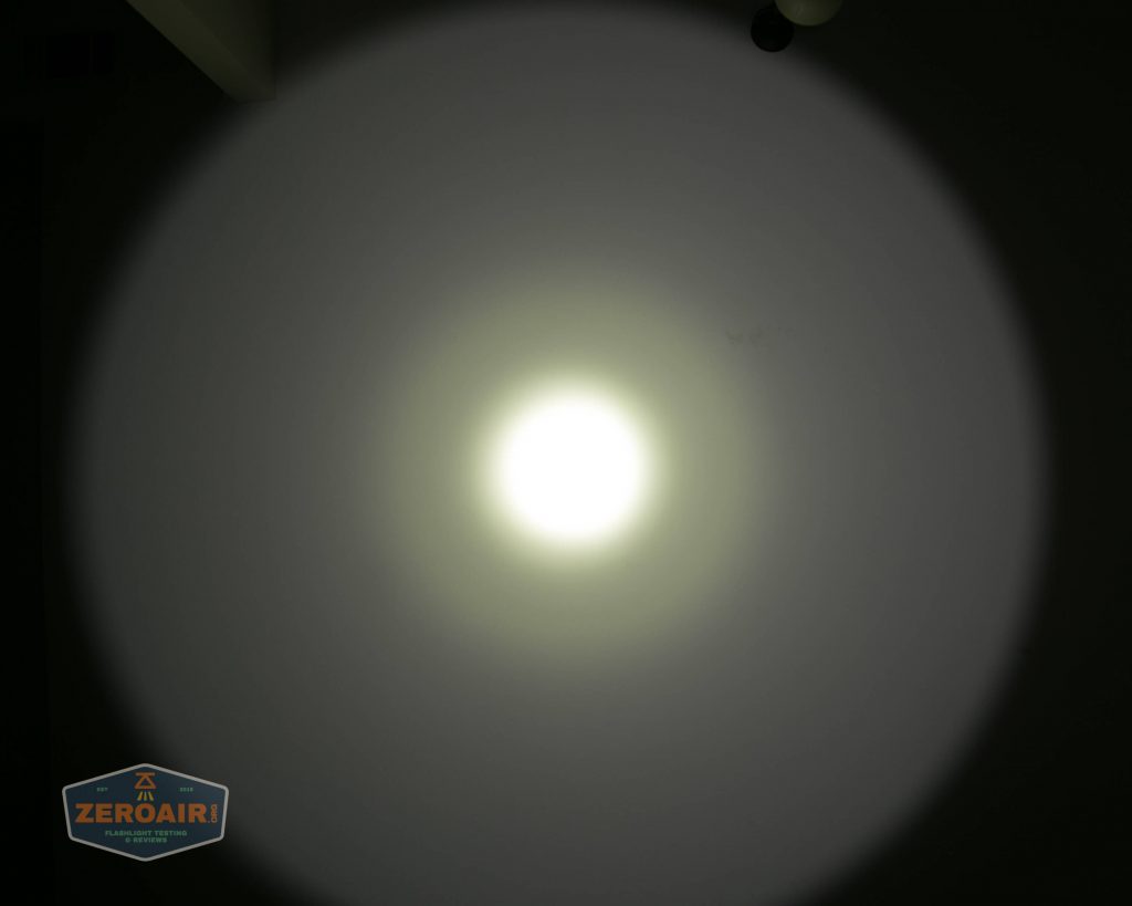 A bright circular beam of white light is projected onto a dark surface, creating a defined central hotspot with a larger, softer outer halo. A small logo labeled ZEROAIR appears in the lower left corner.