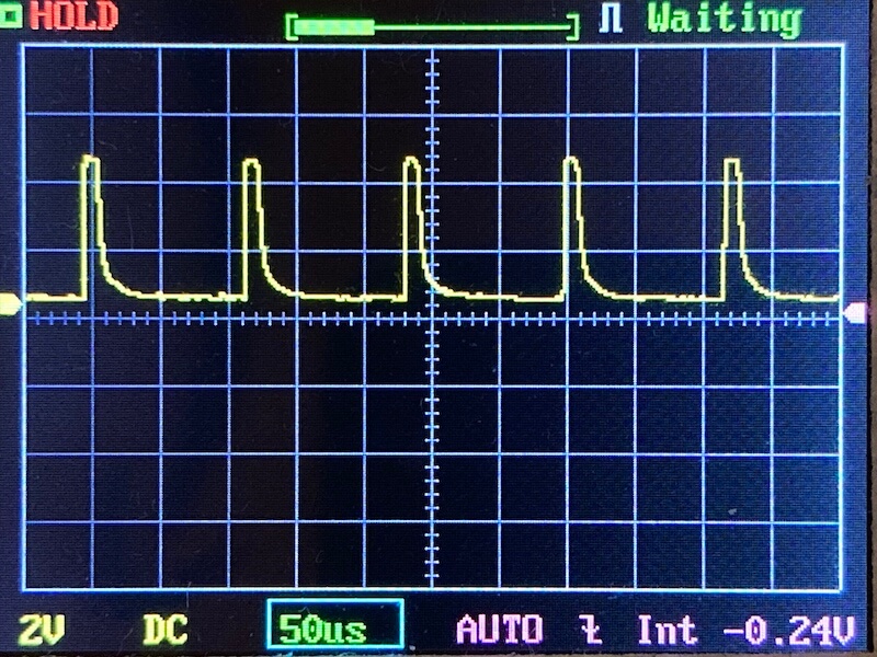 An oscilloscope screen displays a repetitive pulse waveform with five distinct pulses. The settings shown include 2V per division, 50 microseconds per division, and a measured voltage of -0.24V.