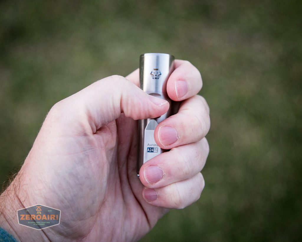 A person holds a small, silver flashlight in their hand against a blurred outdoor background. The flashlight displays the logo of Acebeam and model information near the base.