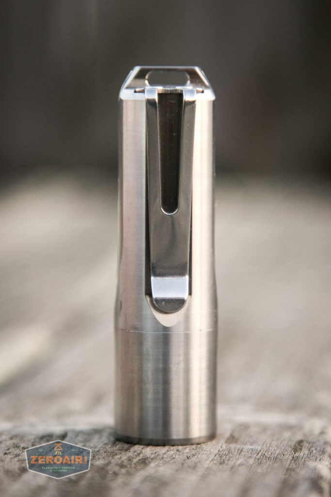 A cylindrical stainless steel object with a metal clip stands upright on a wooden surface. The background is blurred, and a Zeroair logo is visible in the bottom left corner.