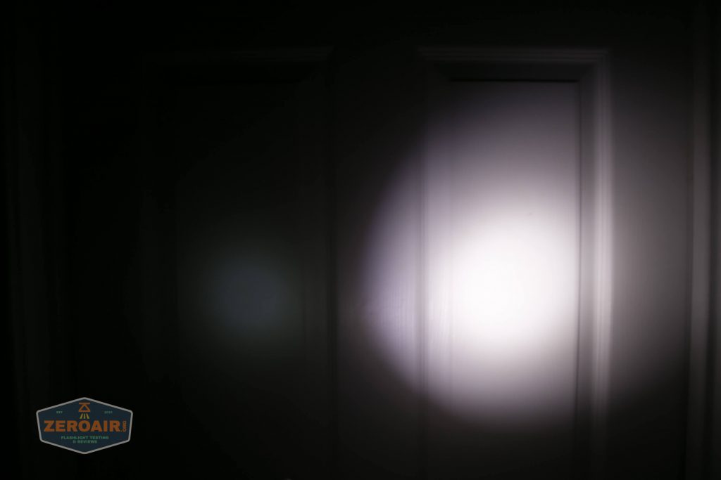 A dark room with a door illuminated by a bright flashlight beam in the center, creating a circular light spot, with a small ZeroAir logo in the bottom left corner.