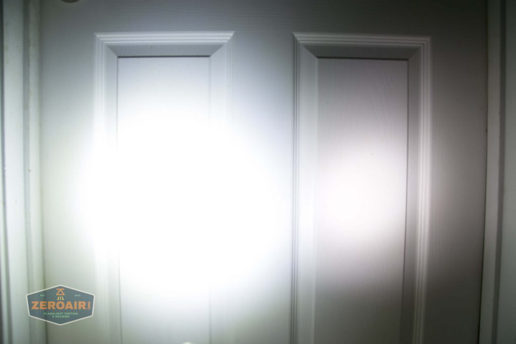 A bright flashlight beam is aimed at a white paneled door, creating a large, round glare in the center. A small logo reading ZEROAIR! is visible in the bottom left corner.