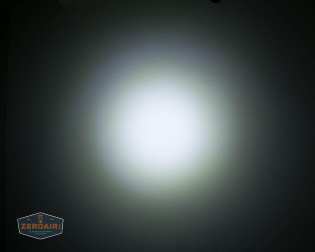 A white flashlight beam creates a circular spot of light on a dark wall, fading gradually at the edges. A small ZeroAir logo appears in the lower left corner of the image.