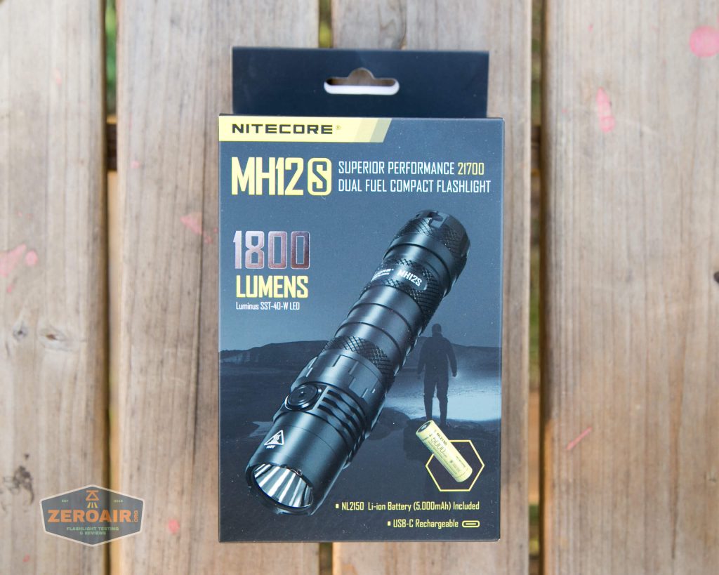 A Nitecore MH12S flashlight box on a wooden surface, showing product features such as 1800 lumens brightness, dual fuel compatibility, and inclusion of a 21700 lithium battery.