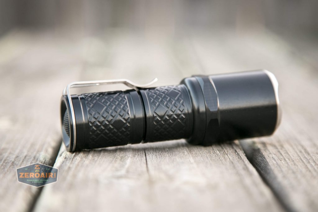 An Oveready P35 Aluminum Black flashlight with a textured grip and hexagonal bezel rests on a weathered wooden surface, its sleek metal clip visible from the side.