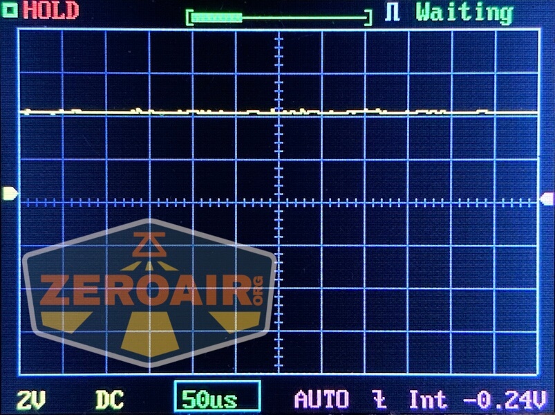 An oscilloscope screen displays a mostly flat yellow waveform. Indicators show settings like 2V DC, 50 microseconds per division, and -0.24V offset. The words “HOLD,” “Waiting,” and “ZEROAIR.org” are visible.