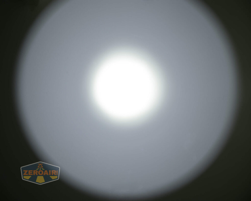 A bright white circular spotlight is centered against a dark background. The light fades outward, creating a gradient. The bottom left corner displays a ZEROAIR logo with a shield design.