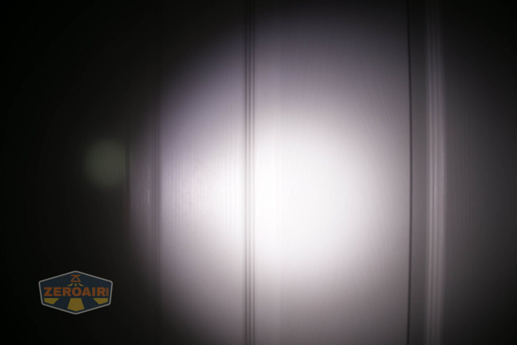 A circular beam of white light is projected onto a vertical, textured white surface with three narrow vertical grooves. The ZeroAir logo is visible in the lower left corner.