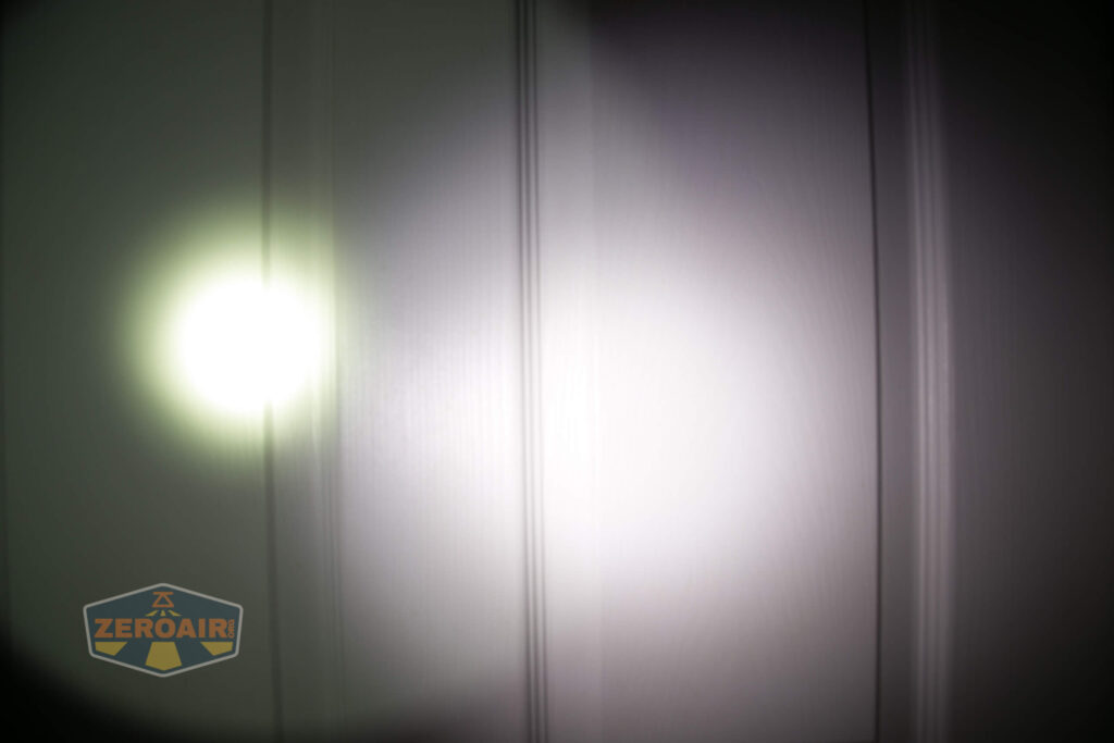 A flashlight beam is projected onto a vertical surface, creating a bright circular spot with a faint yellowish tint. A logo with the text “ZeroAir” appears in the lower left corner.