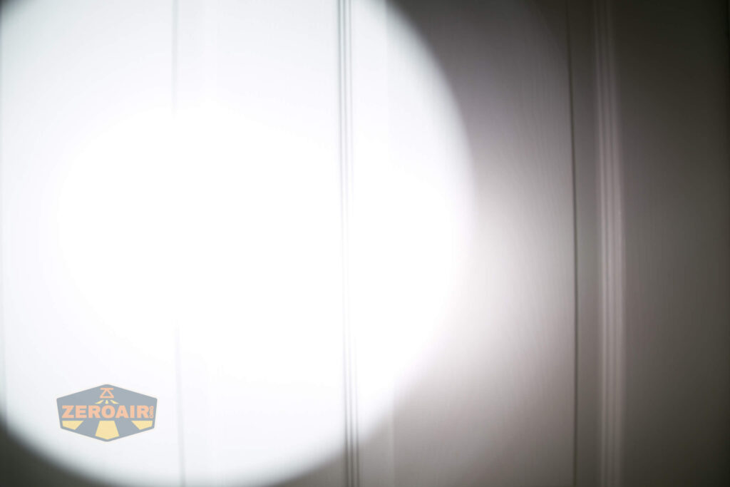 A bright flashlight beam shines on a white paneled surface, creating a circular area of intense light. The ZeroAir logo appears in the bottom left corner of the image.