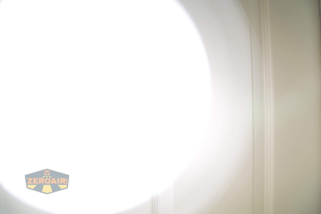 A bright white circle of light dominates the center and left side of the image, washing out most details. On the lower left, a small logo with the text ZeroAir is visible. Vertical lines are faintly seen in the background.