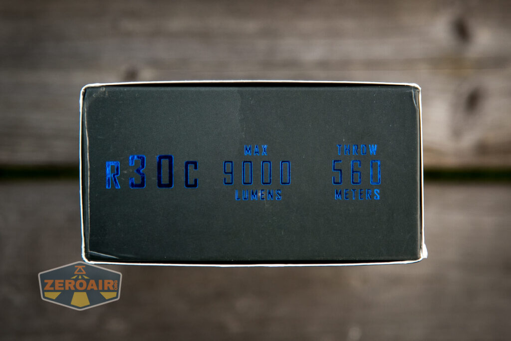 A close-up of a product box shows text reading R30C, Max 9000 Lumens, Throw 560 Meters in blue lettering. The background is out of focus, and a ZeroAir logo appears in the bottom left corner.