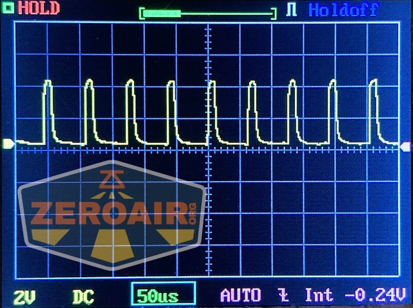 An oscilloscope screen displays a repeating yellow waveform with sharp peaks. The grid shows voltage and time values, alongside interface labels like HOLD, Holdoff, 2V, 50µs, and -0.24V. A ZeroAir logo and Lumintop GT Nano Brass overlay complete the image.