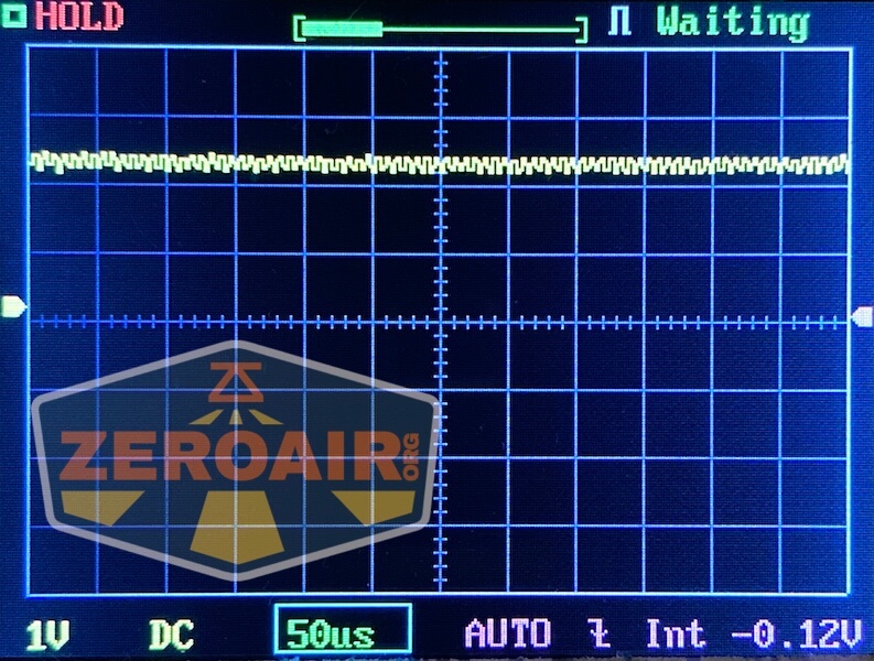 An oscilloscope screen displays a stable, flat waveform with minor noise. The horizontal scale is set to 50 microseconds per division and the vertical scale to 1 volt per division. The word WAITING is shown at the top right.