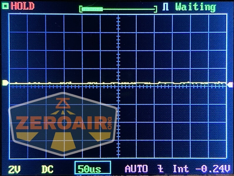 A digital oscilloscope screen shows a mostly flat yellow waveform near zero volts, with grid lines and measurement settings. The display includes the ZeroAir logo in the lower left corner.
