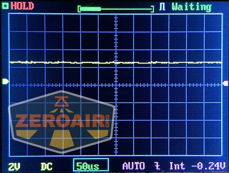 Oscilloscope screen displaying a mostly flat yellow waveform centered near zero volts. The screen shows HOLD, Waiting, and settings including 2V DC, 50µs time base, and an average voltage of -0.24V. Zeroair.org logo visible.