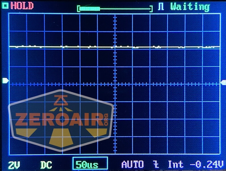 Oscilloscope screen showing a mostly flat horizontal waveform near zero volts, with grid lines, voltage and time settings displayed. The words “HOLD” and “Waiting” appear at the top, and a ZeroAir logo is visible on the left.