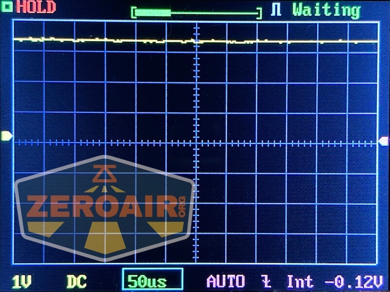 An oscilloscope screen displays a mostly flat yellow waveform near the top, with grid lines and measurement indicators. The screen shows HOLD, Waiting, and ZEROAIR logo at lower left. Settings: 1V DC, 50μs, AUTO, -0.12V.