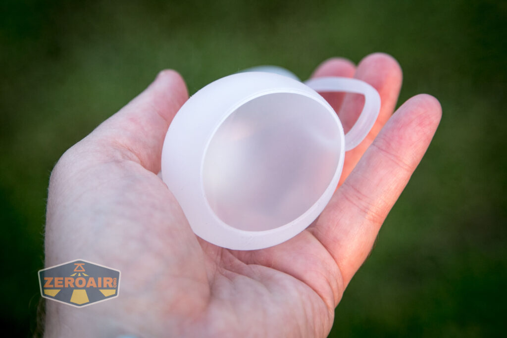 A hand holds a small, translucent, frosted silicone cup with a handle. The background is blurred green, and a “ZeroAir” logo appears in the corner of the image.